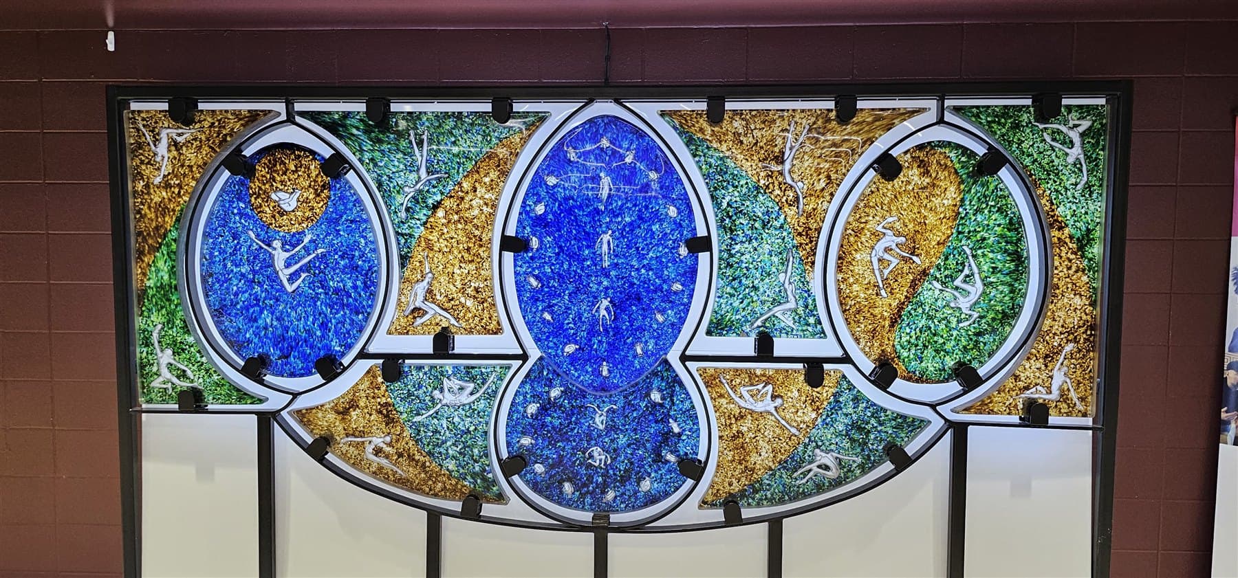 The second Townsend mural: interlocking oval panels of cobalt blue, green and gold fused glass, with pale figures caught mid-movement across them