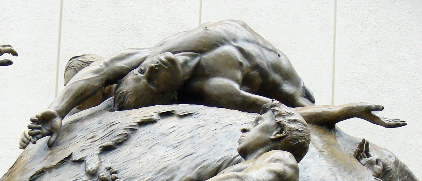 Detail across the top of the globe, where several bronze figures lie over the modelled continents with arms outstretched